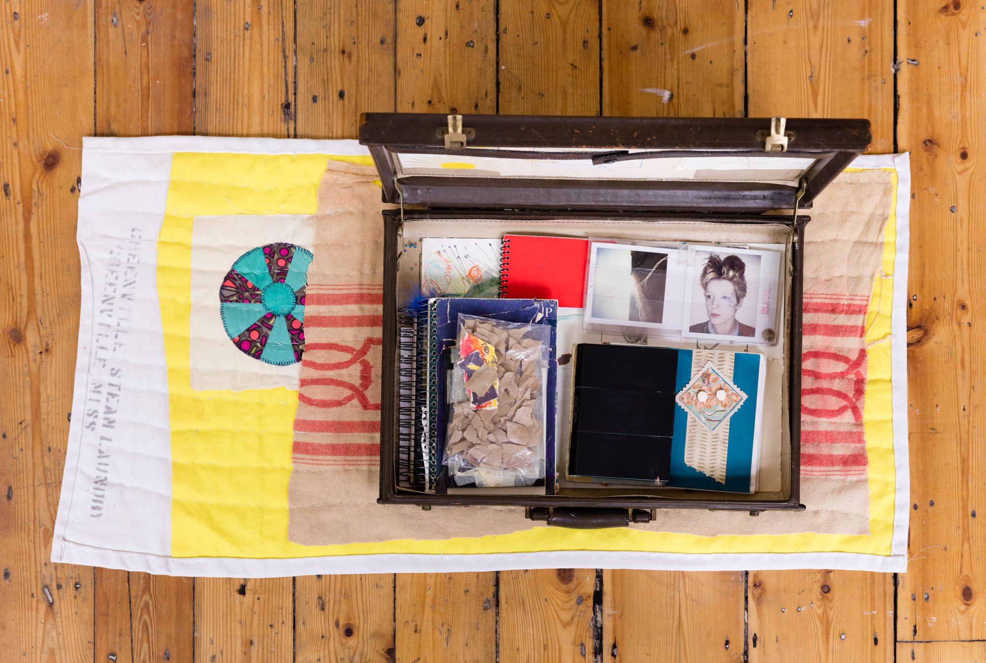 Susan Cianciolo, Briefcase Kit, briefcase, ink and pencil on paper, torn brown paper in plastic bag, archival books from: Love Life, Run 8, Run 10, Small Things &amp; Games and Museum for Moderne Kunst Costumes [book] on handmade quilt by Coulter Fussell, 40.64 x 46.99 x 96.52 cm (16 x 18 1/2 x 38 in), 1997 – 2015