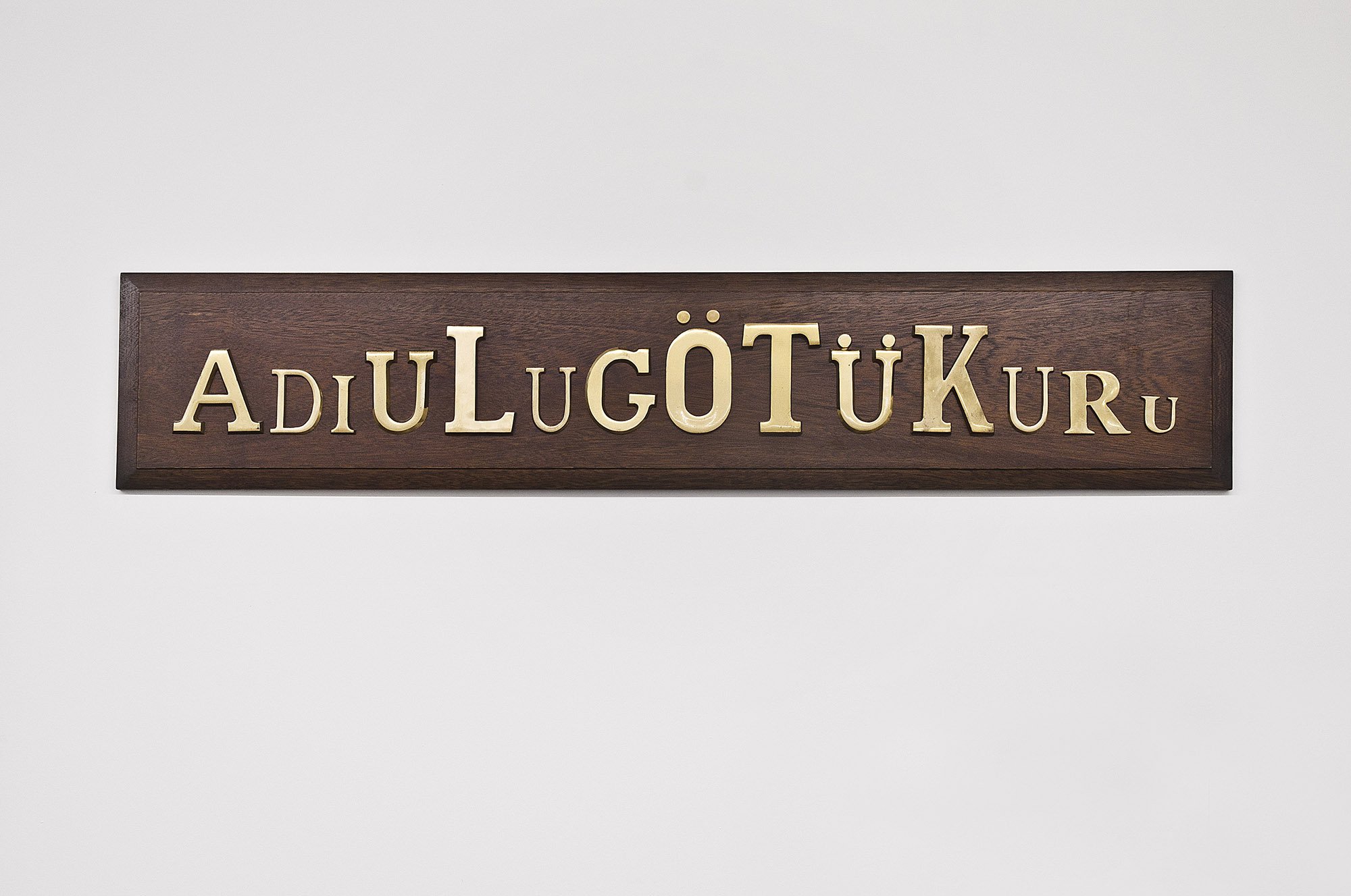 Banu Cennetoğlu, Adı Ulu Götü Kuru (great name dry ass), bronze letters on wood, 150 x 30 cm (59 x 11 3/4 in), 2010. Installation view, SAMPLE SALE / 2010 BC, Rodeo, Istanbul, 2010