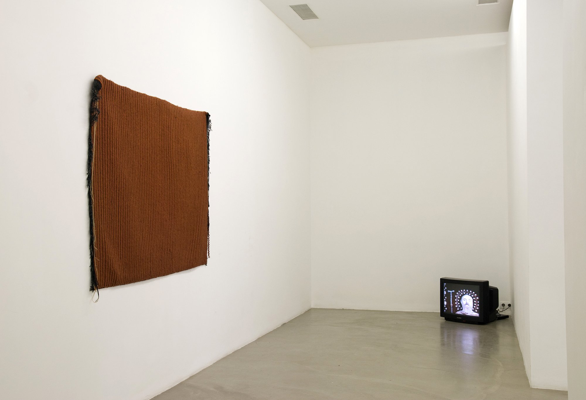 (Left) Cevdet Erek, Shore Scene Soundtrack, carpet &amp; video (2006) &amp; three drawings &amp; one book, 2008. (Right) Sergei Paradjanov, The Color of Pomegranates, film on monitor, 88 min., 1969. Installation view, Altogether Elsewhere, Rodeo, Istanbul, 2010