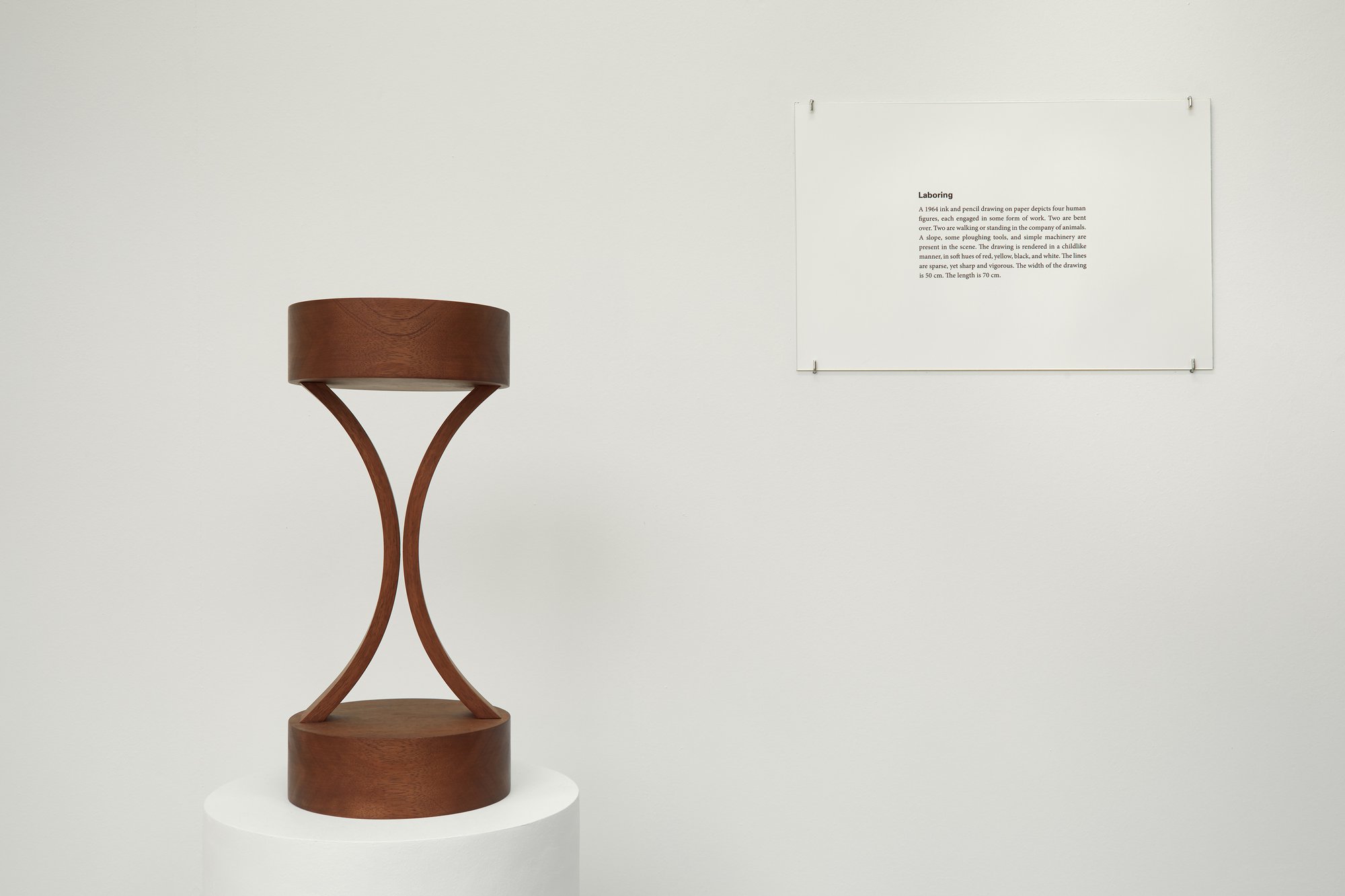 Iman Issa, Labouring (study for 2012), mahogany sculpture, text panel under glass, white plinth, sculpture: 39.4, Ø 18 cm (15 1/2, Ø 7 in), plinth: 95.2 x Ø 30 cm (37 1/2 x Ø11 3/4 in), 2012
