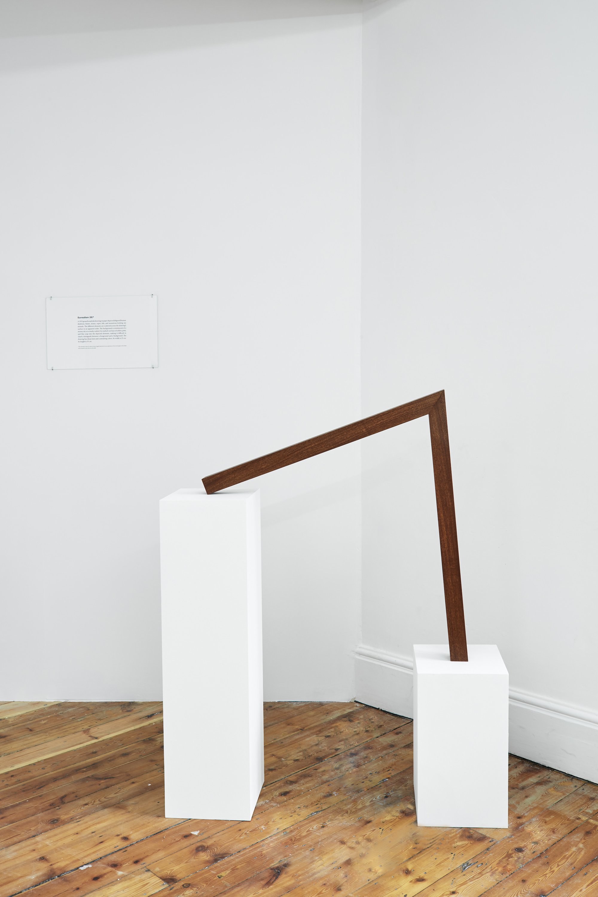 Iman Issa, Surrealism III (study for 2014), mahogany sculpture, text panel under glass and two white plinths, sculpture: 79.6 x 75 x 5 cm, small plinth: 45 x 25 x 25 cm, large plinth: 93.3 x 25 x 25 cm, 2014
